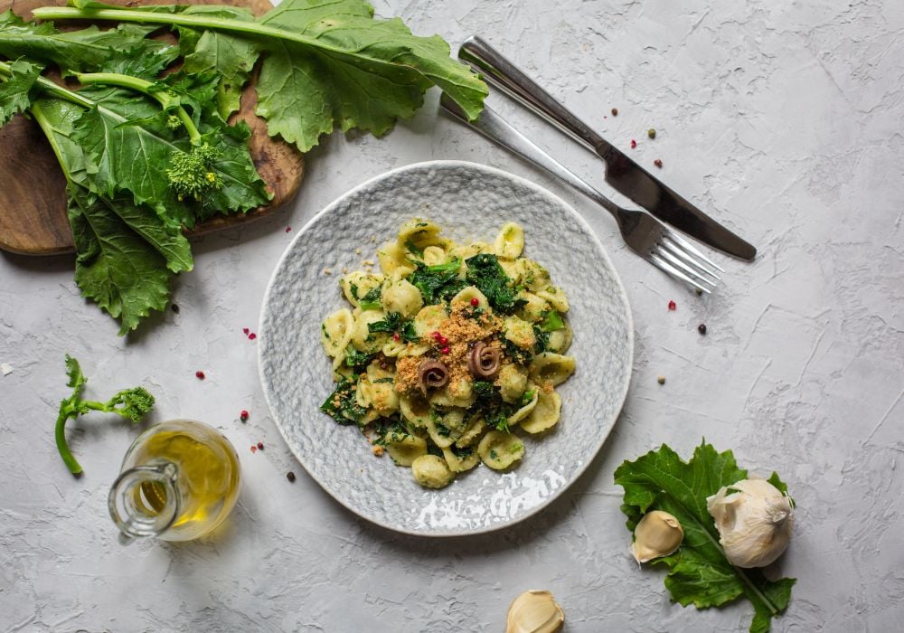 The delicious orecchiette is on a ceramic plate with herbs and olive oil on the table.